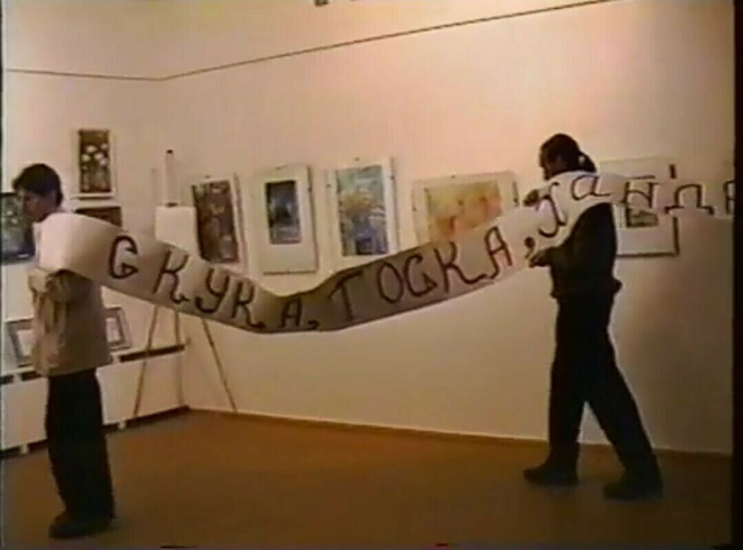 Two people carrying a long hand-painted banner through an art gallery in Apatity